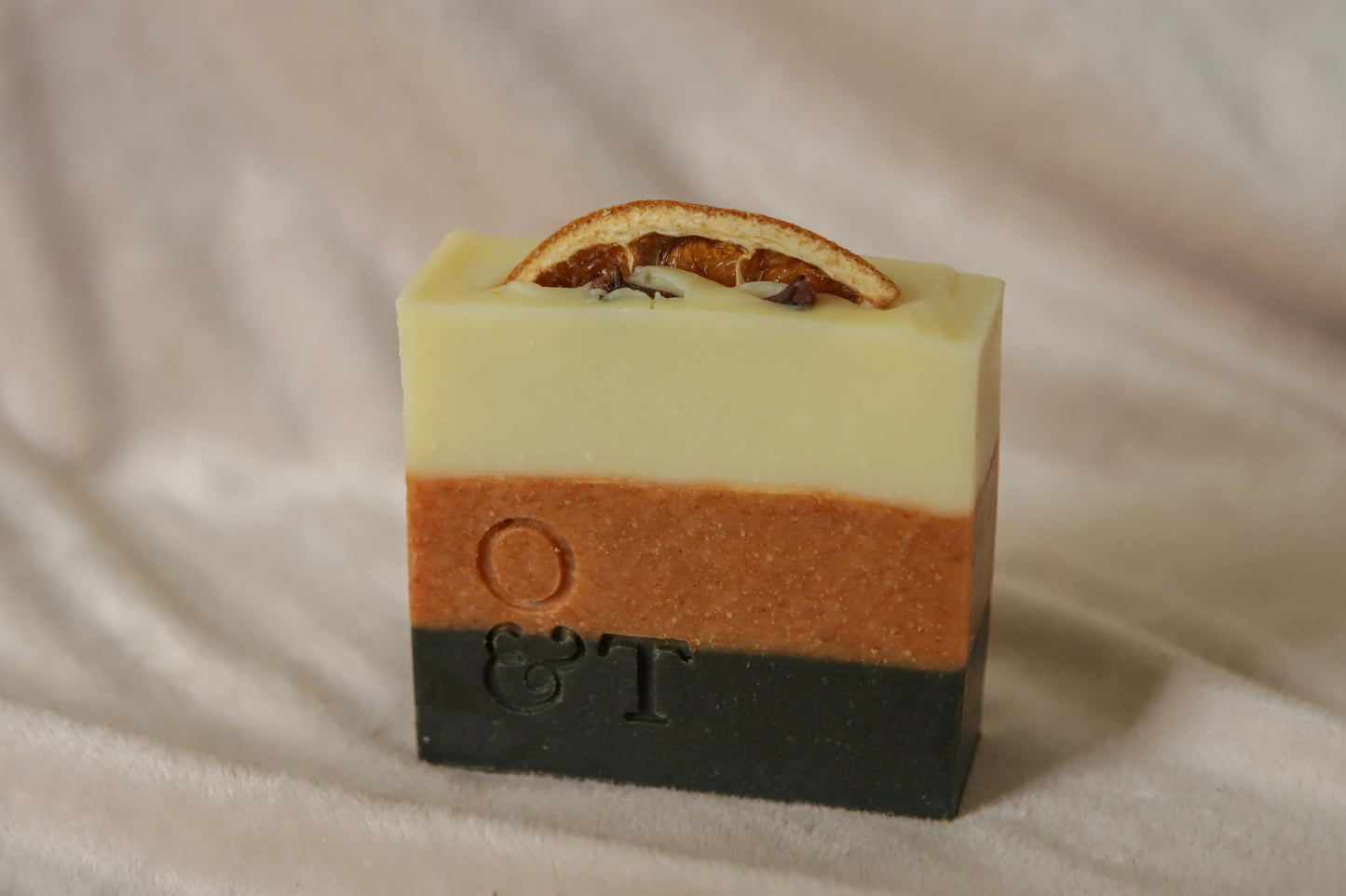 Spice soap bar, black orange creamy with striped colours, topped with an orange and cloves and stamped with the o&t logo