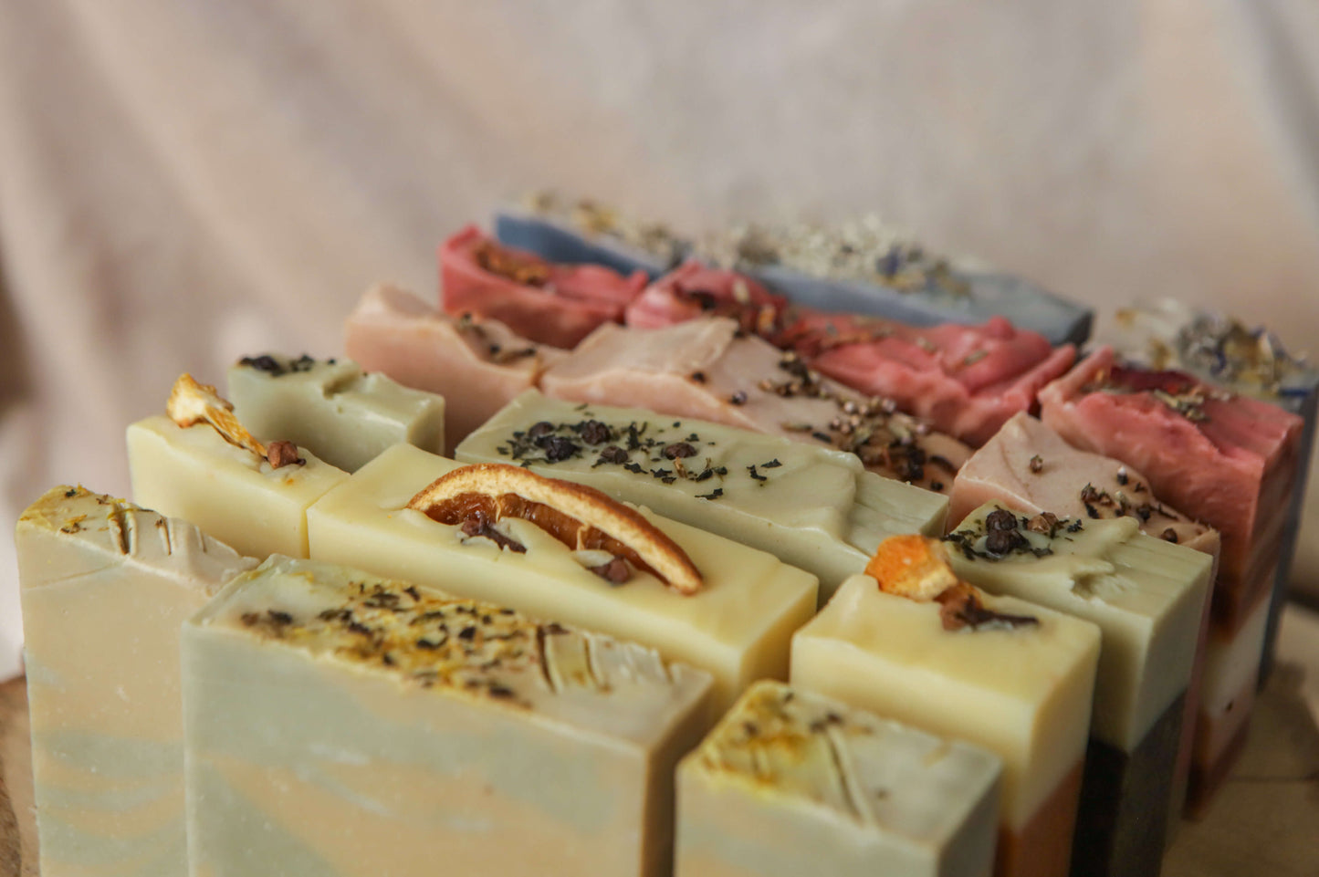 six naturally coloured soaps with different colours, toppings and scents, in the order, green and yellow for mentha, beige and orange for spice, light green and dark green for fern, pink for heather, dark pink for flora, and blue for moss, each soap has three different sizes displayed too, the left row has thin quarter bars, full big bars in the middle, and half size bars on the right