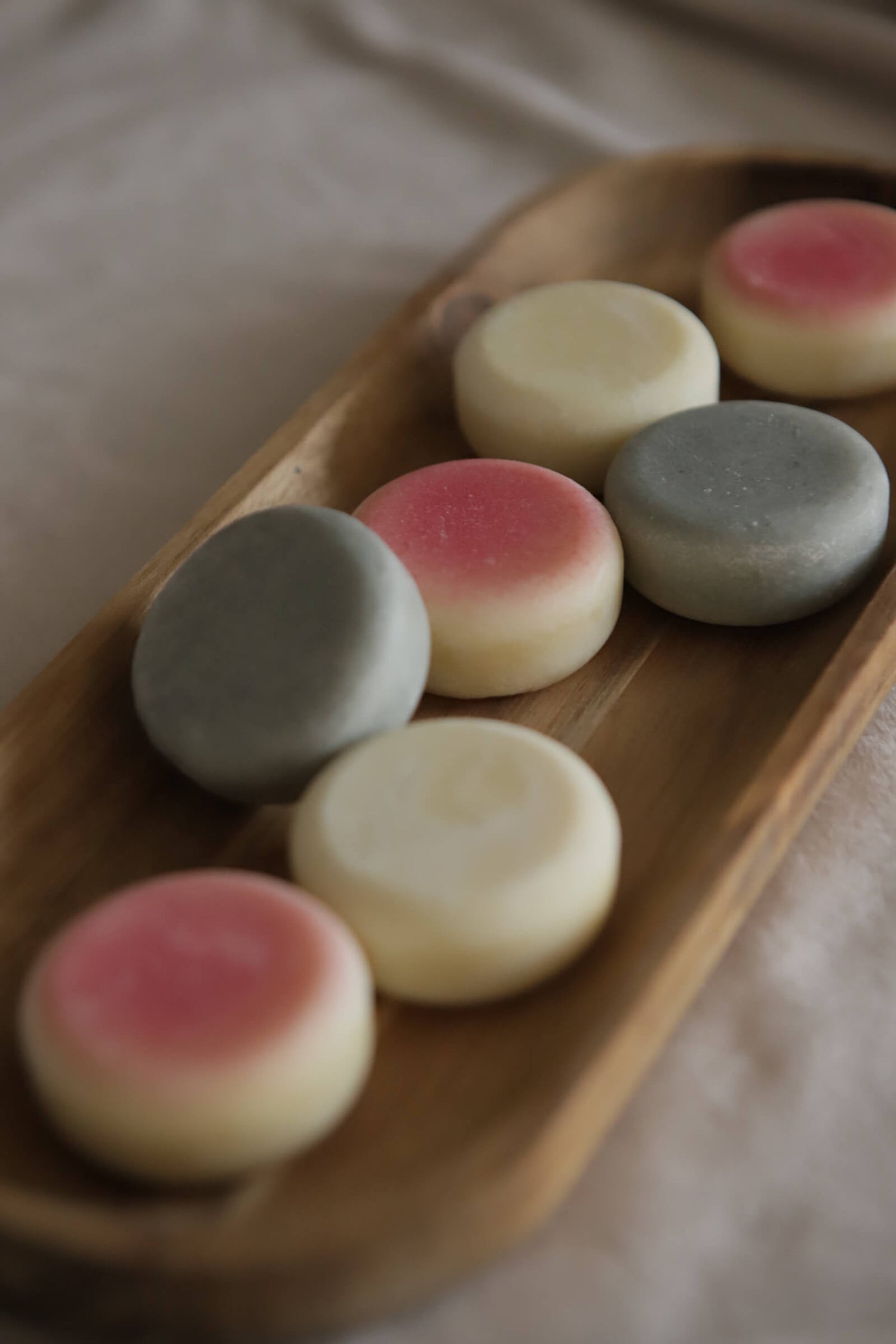 Mixed colours of mini lotion bars, white - nude, pink - sol, blue - heather on decorative wooden tray