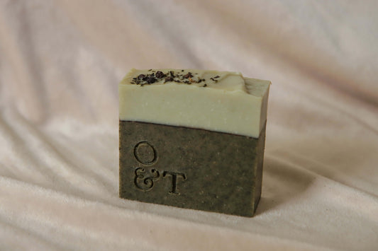 Fern soap bar, dark green base with a light green top and decorated with black peppercorns and nettle powder, stamped with the o&t logo