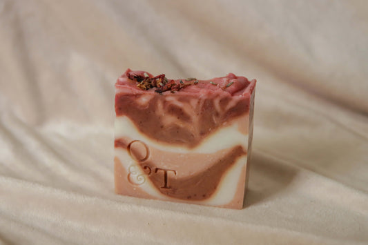 Flora soap bar out of packaging, red, pink and creamy white swirls, topped with rose petals and lavender and stamped with the O&T logo