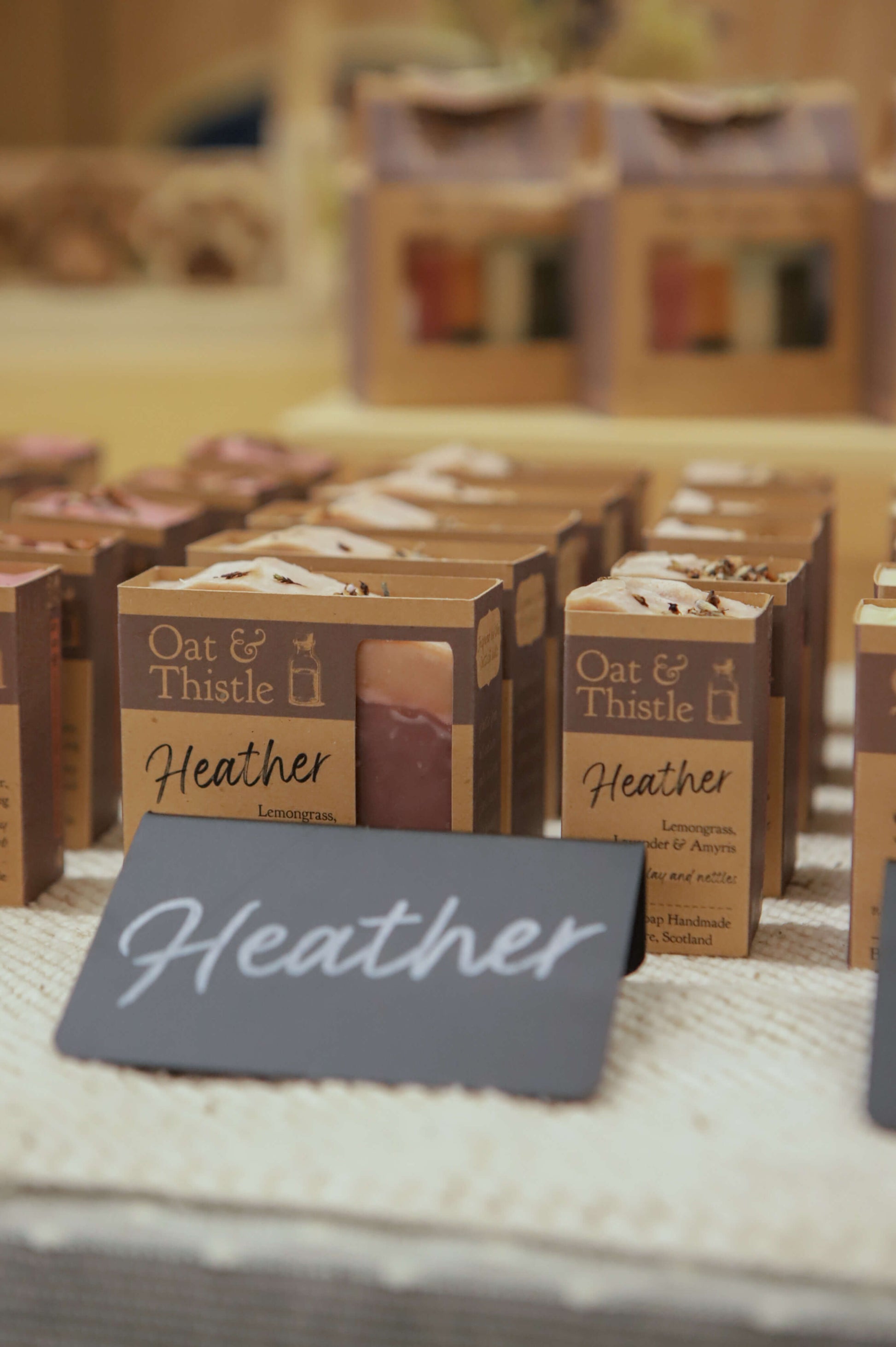 Heather soap in its Kraft packaging stacked up in a row on a market table