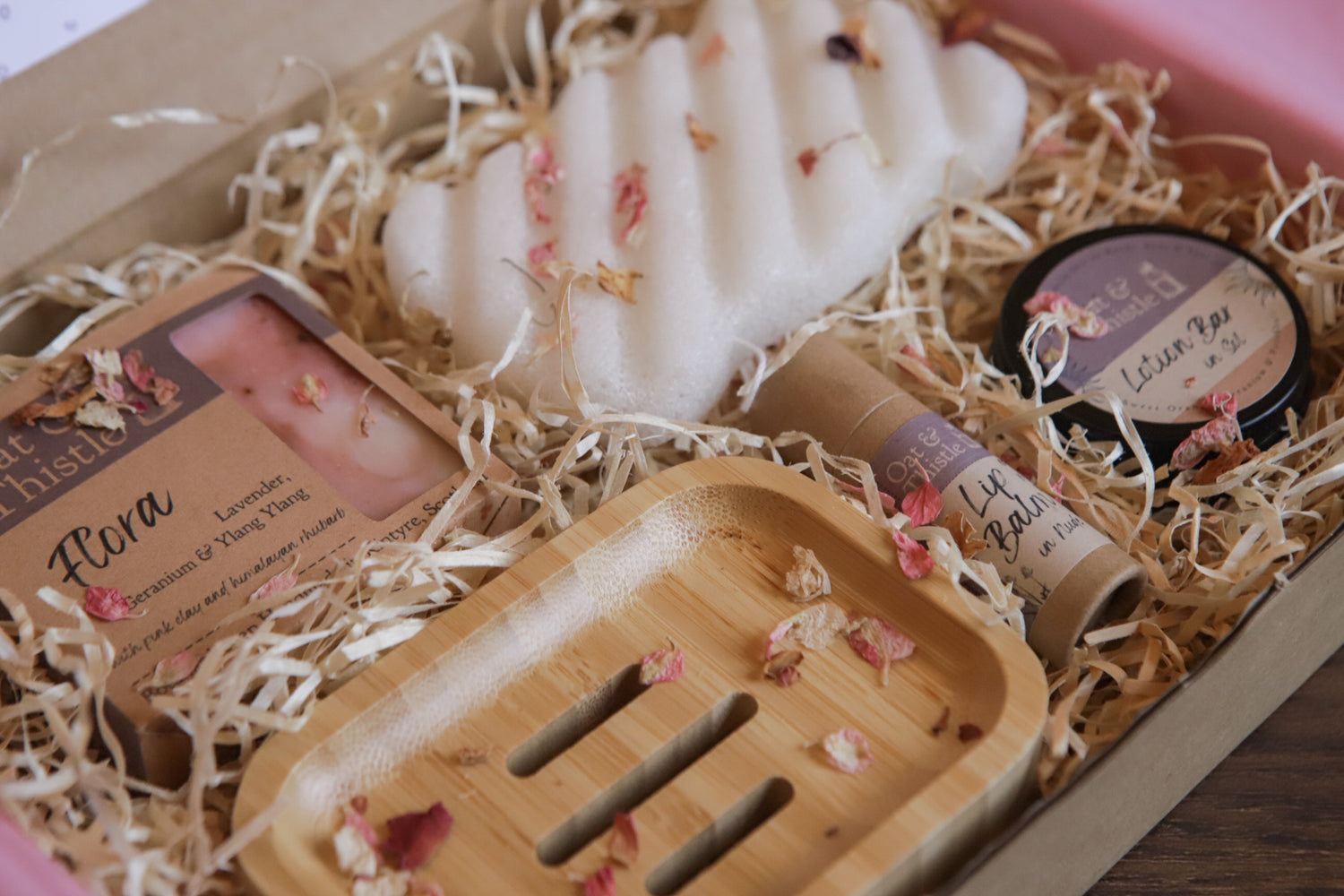 A Kraft gift box with o&t products (soap, dish, sponge, lip balm, lotion bar) nestled In wood wool and presented beautifully with flower petals