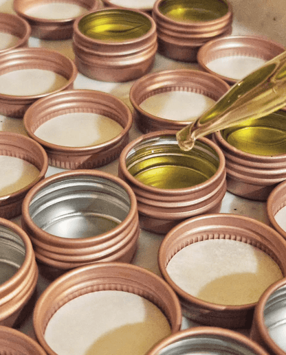 Pink lip balm tins with liquid oil lip balm base being poured in
