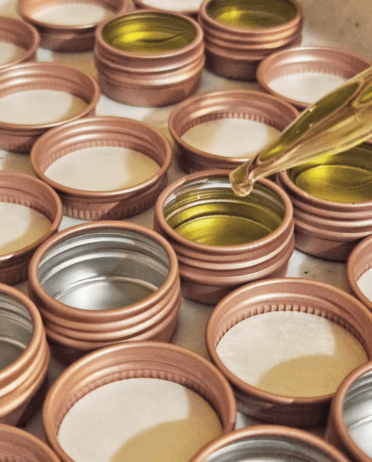 Pink lip balm tins with liquid oil lip balm base being poured in